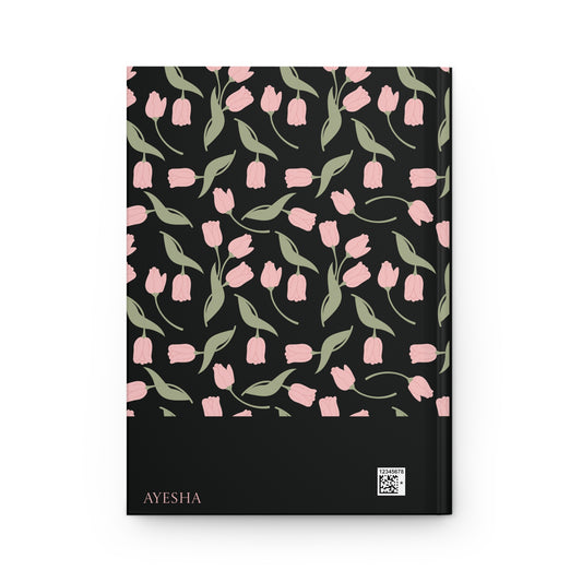 Back cover of a black Qur'an journal with a personalizable name "AYESHA".  The back cover features soft pink floral and leaf artwork.